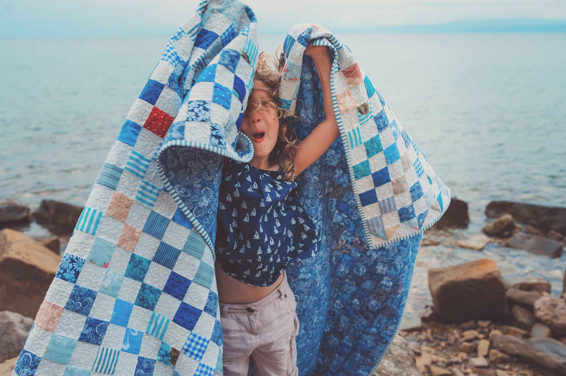 AccuQuilt brand storytelling — a child wrapped in a finished quilt by the water, demonstrating the emotional outcome the cutters help create